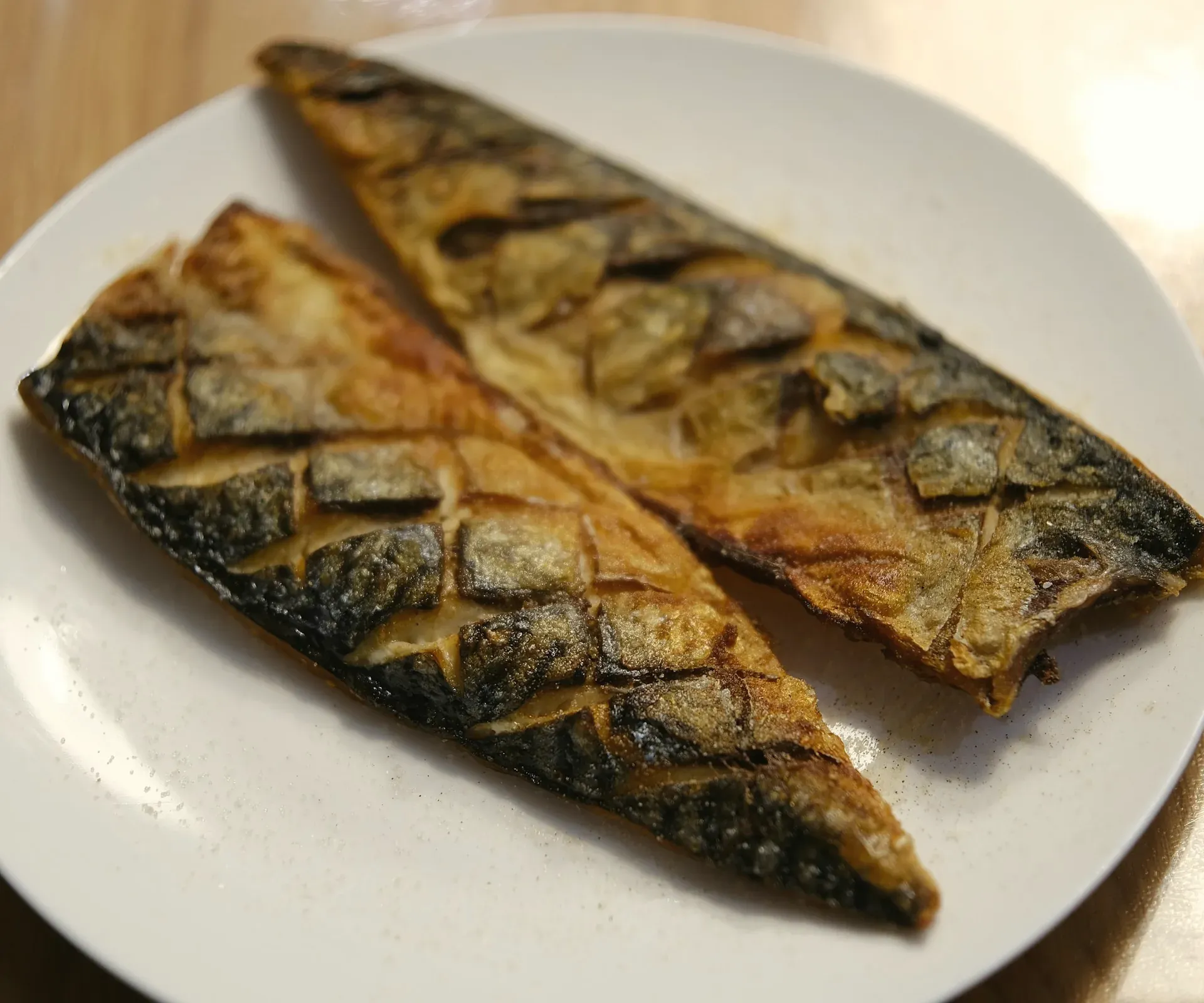 Two scored mackerel fillets grilled golden on a white plate