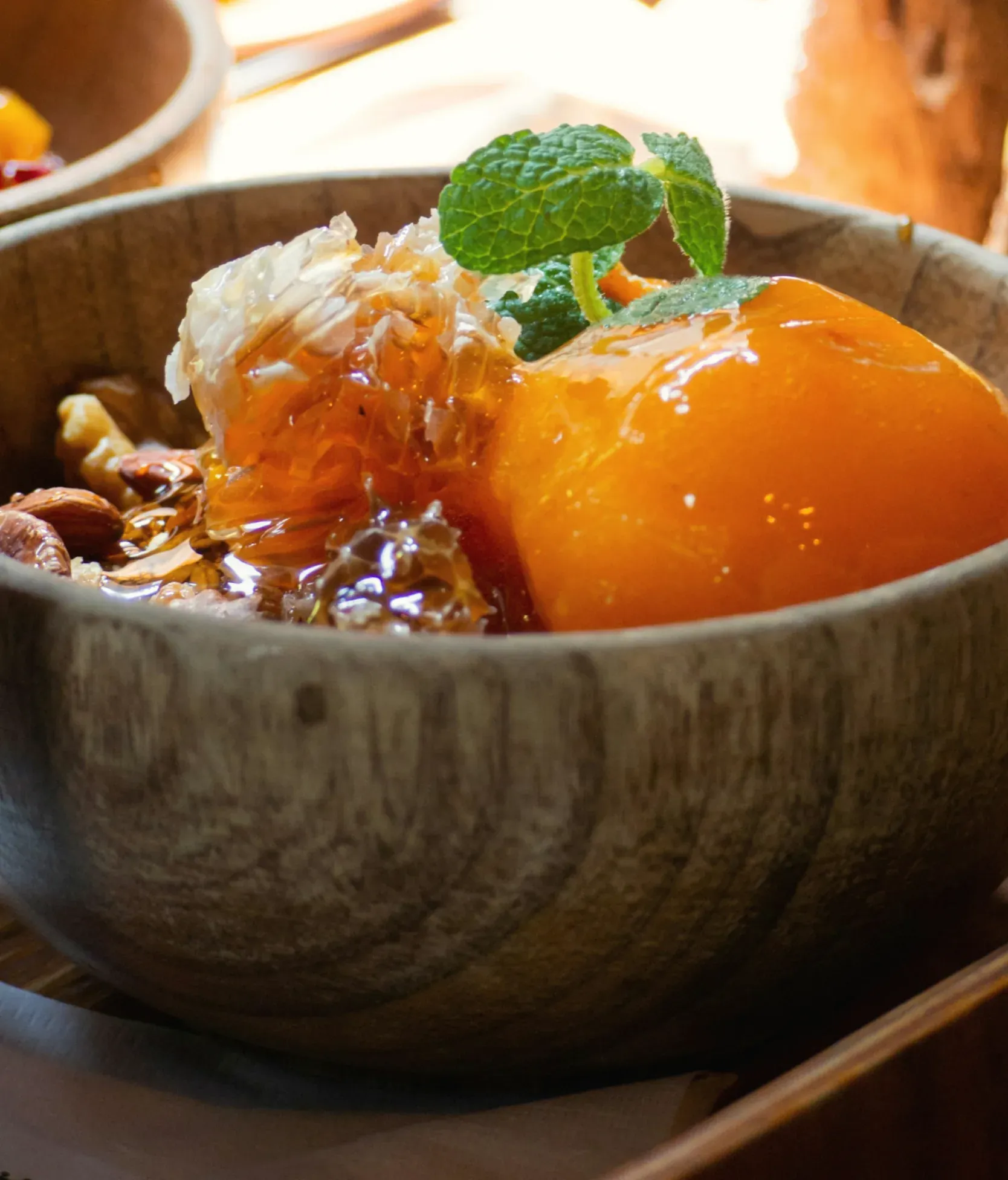 A whole soft-ripe persimmon with honeycomb, almonds, walnuts and mint in a wooden bowl