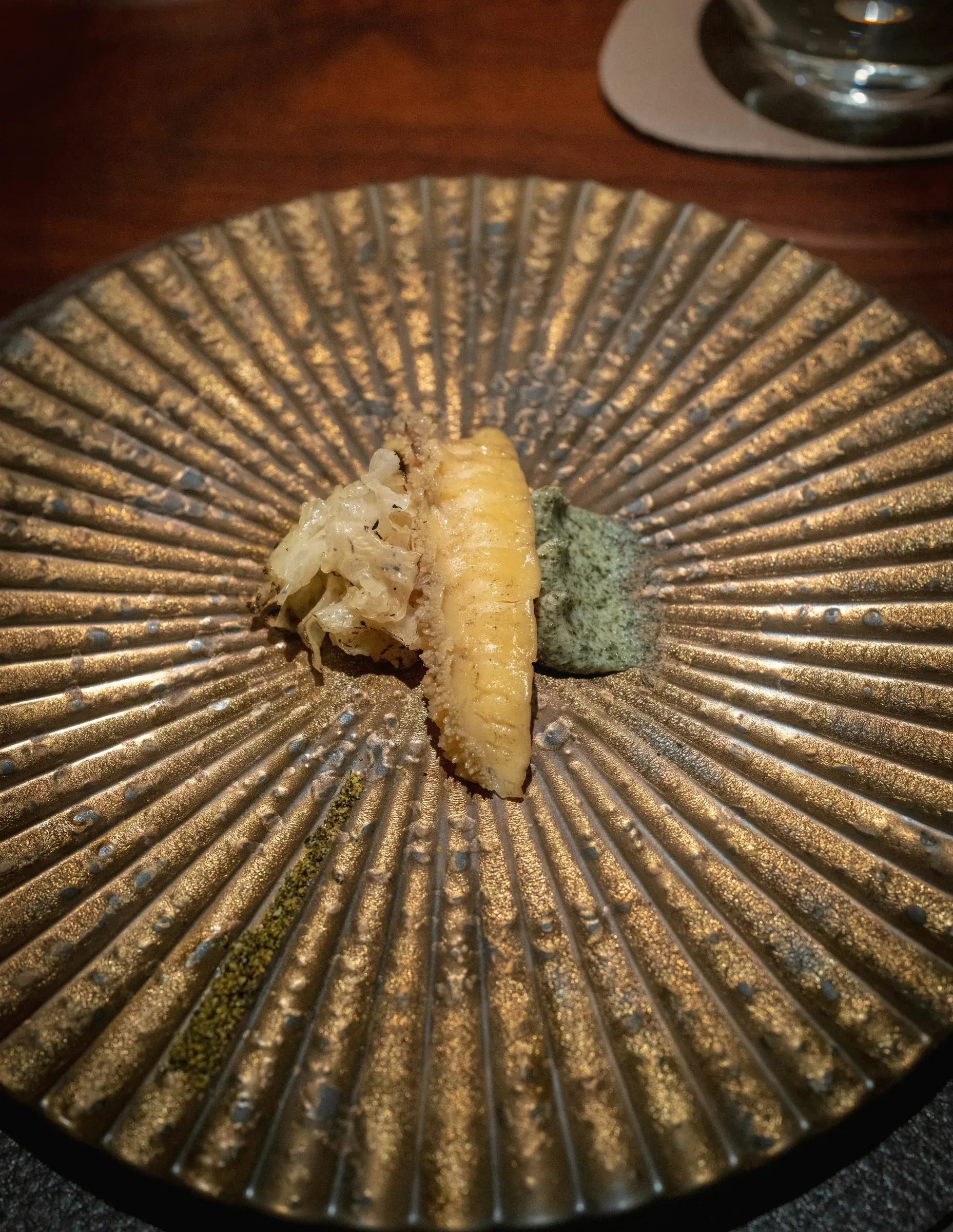 A golden piece of tempura and a green perilla sauce on a ridged bronze-glazed plate