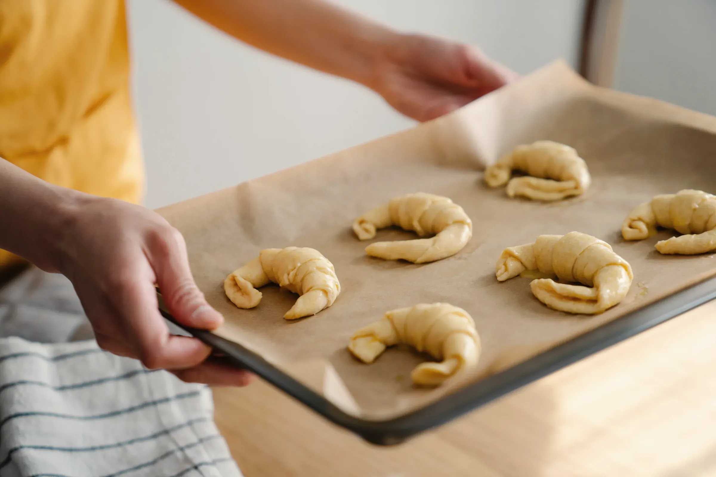 A baker carrying a tray of shaped croissants to the oven
