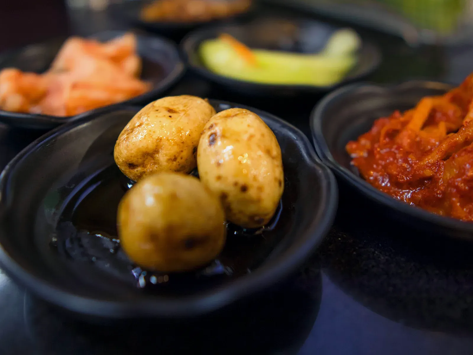 Small dark bowls of kimchi, pickles and soy-braised potatoes