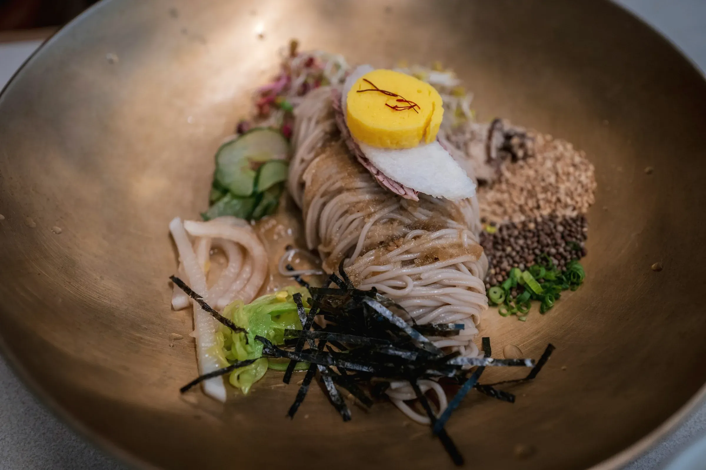 Buckwheat noodles with a cured yolk, seaweed, cucumber and toasted grains in a wide brass bowl