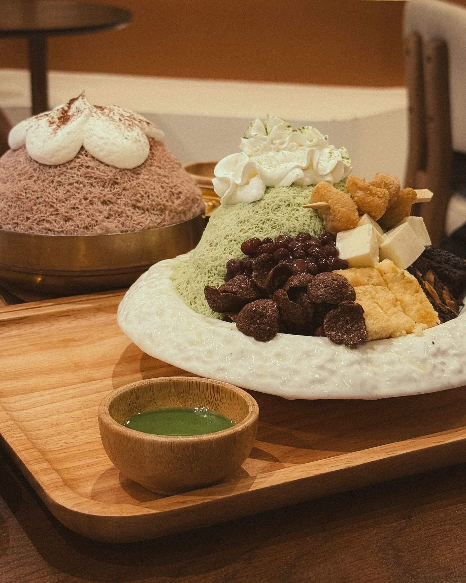 Green tea and cocoa bingsu with red bean, rice cake and cream on a wooden tray