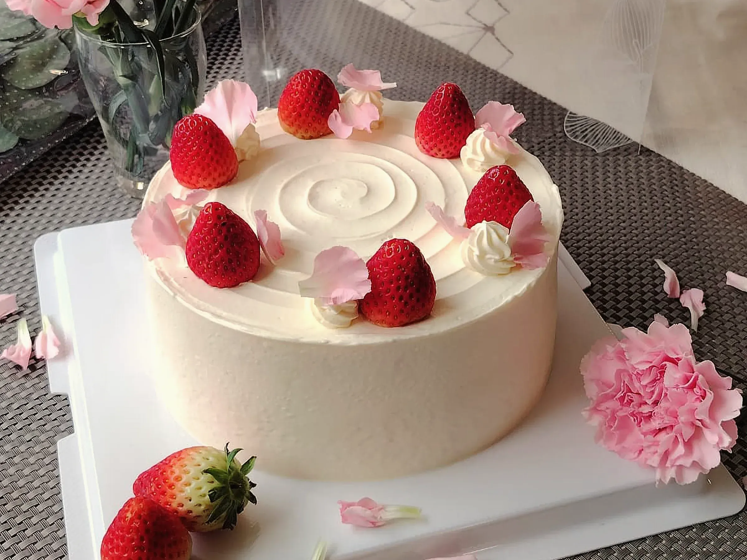 A whole strawberry fresh cream cake with smooth white sides, piped cream and strawberries on top
