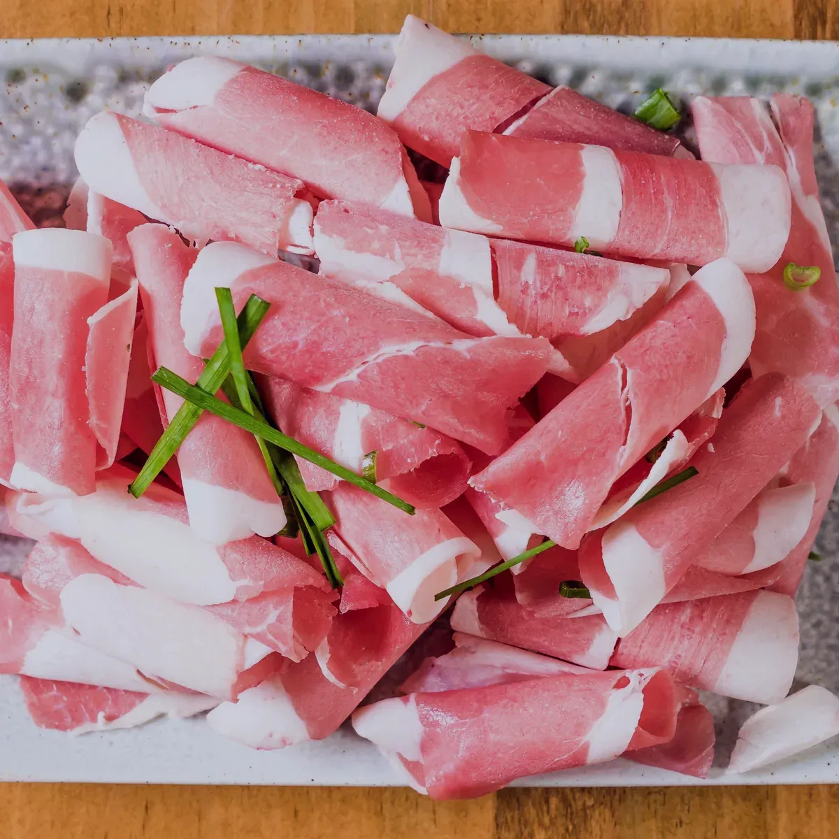 Rolled paper-thin slices of brisket on a speckled plate