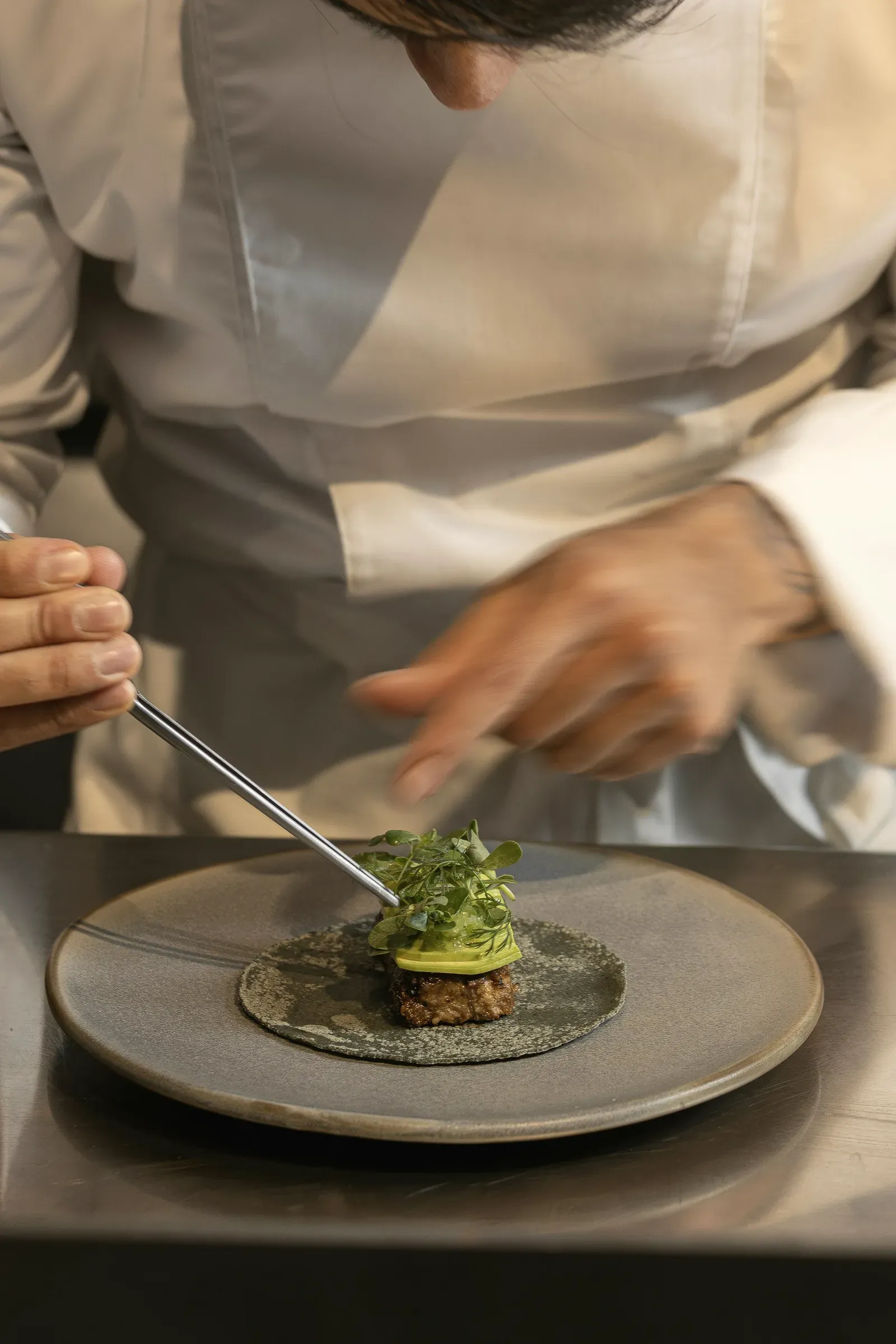 The chef finishing a plate with tweezers at the pass