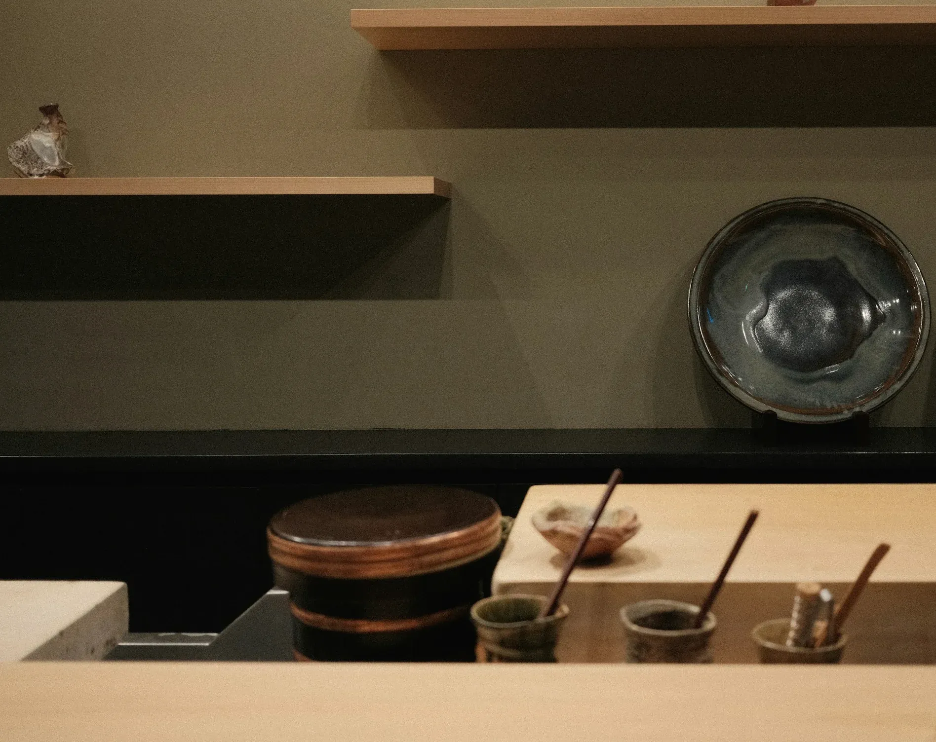 The pale hinoki chef’s counter, stoneware cups and a glazed platter on the shelf behind it