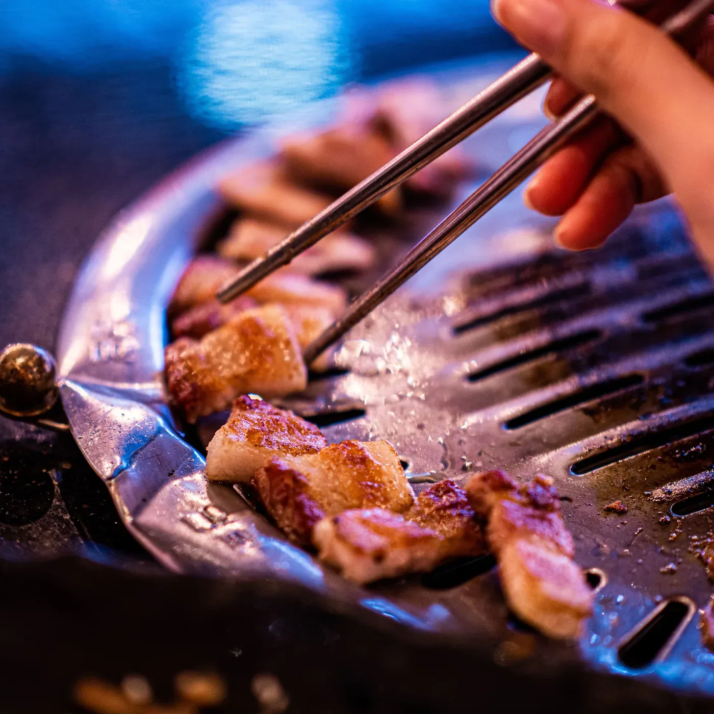 Pork belly turned with chopsticks on a dome grill