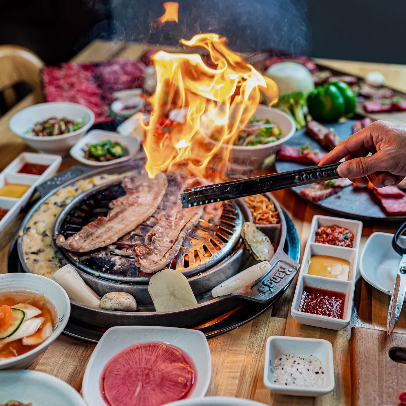 Marinated galbi flaming on a charcoal grill, tongs and banchan around it