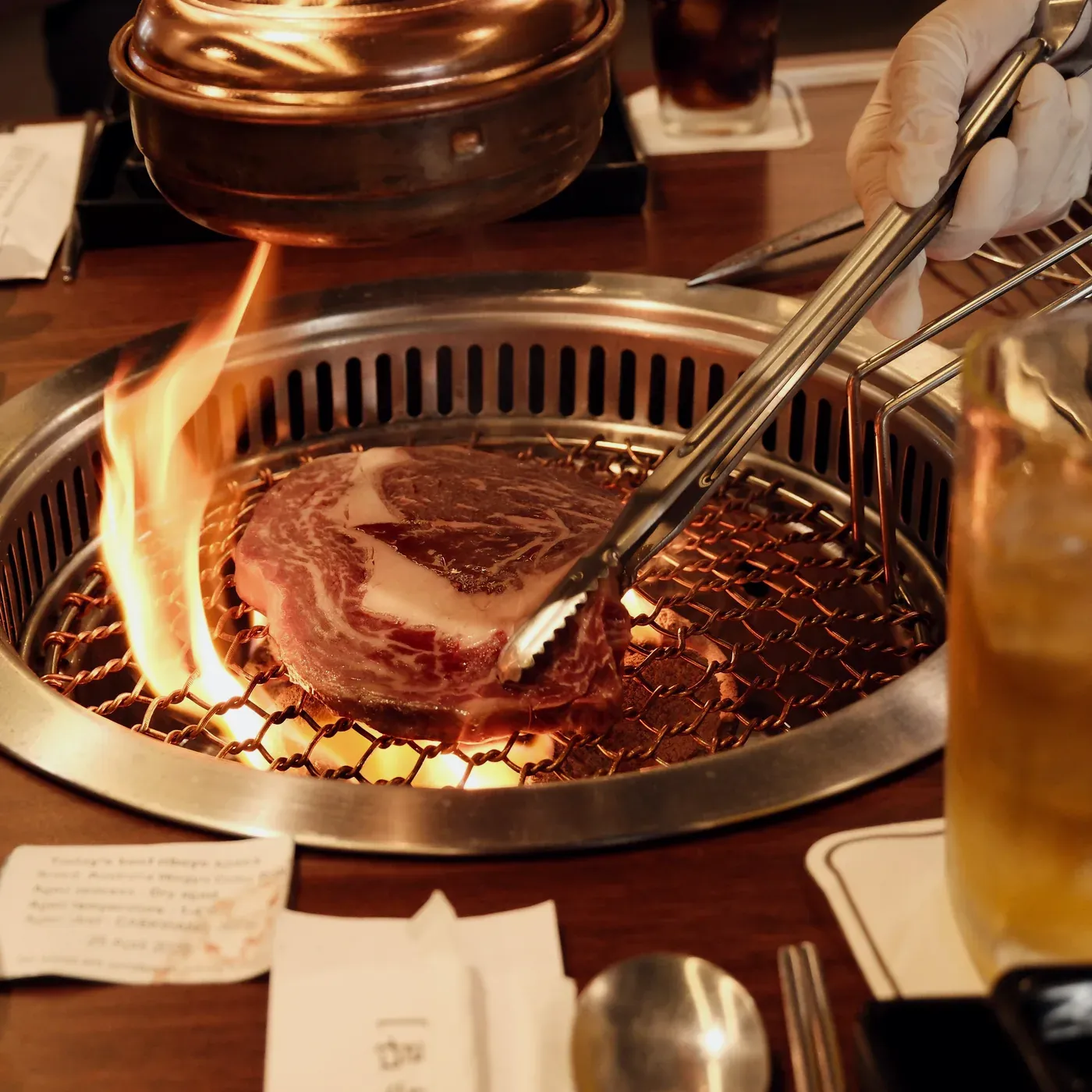 Prime ribeye over charcoal, flames at the edge of the grill
