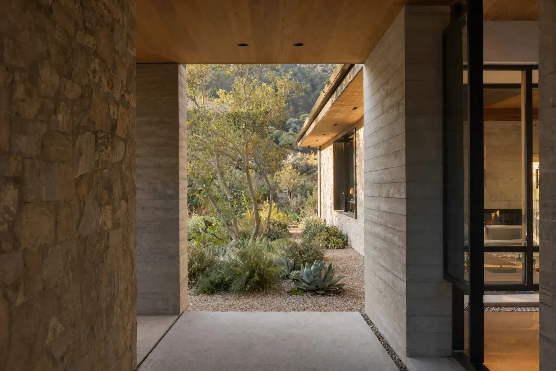 A stone and concrete entry opening toward a sunlit courtyard garden