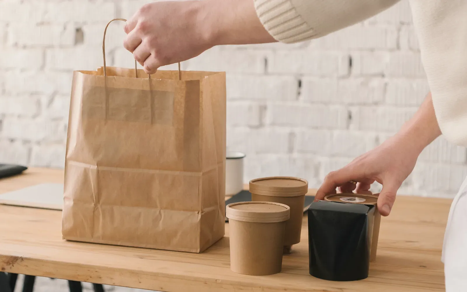Lidded takeout cups and a noodle box going into a paper bag