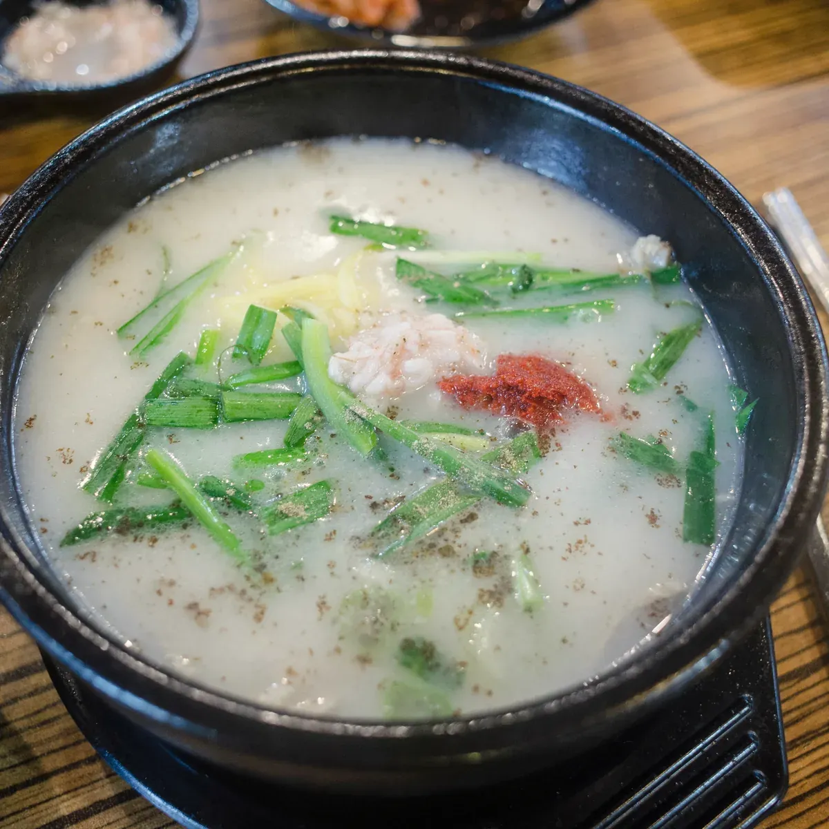 Milky pork bone soup with chives and red seasoning in a black earthenware bowl