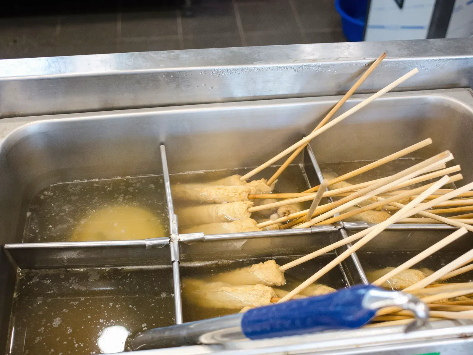 Fish cake skewers simmering in broth in a steel cooker