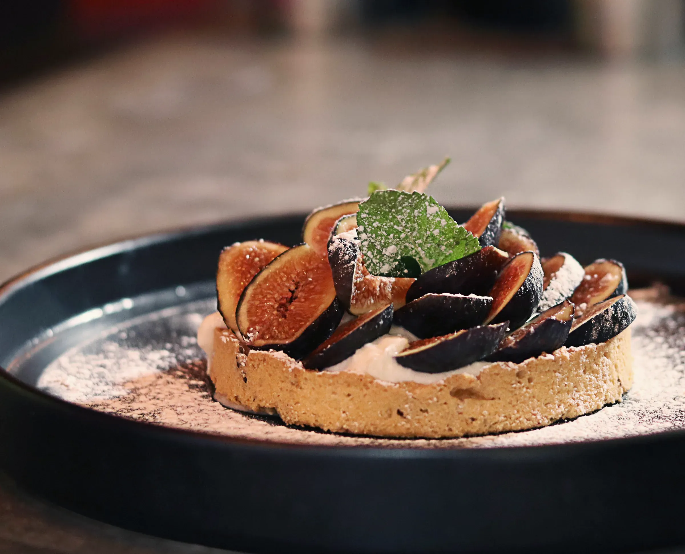 A custard tart topped with halved fresh figs on a dark plate
