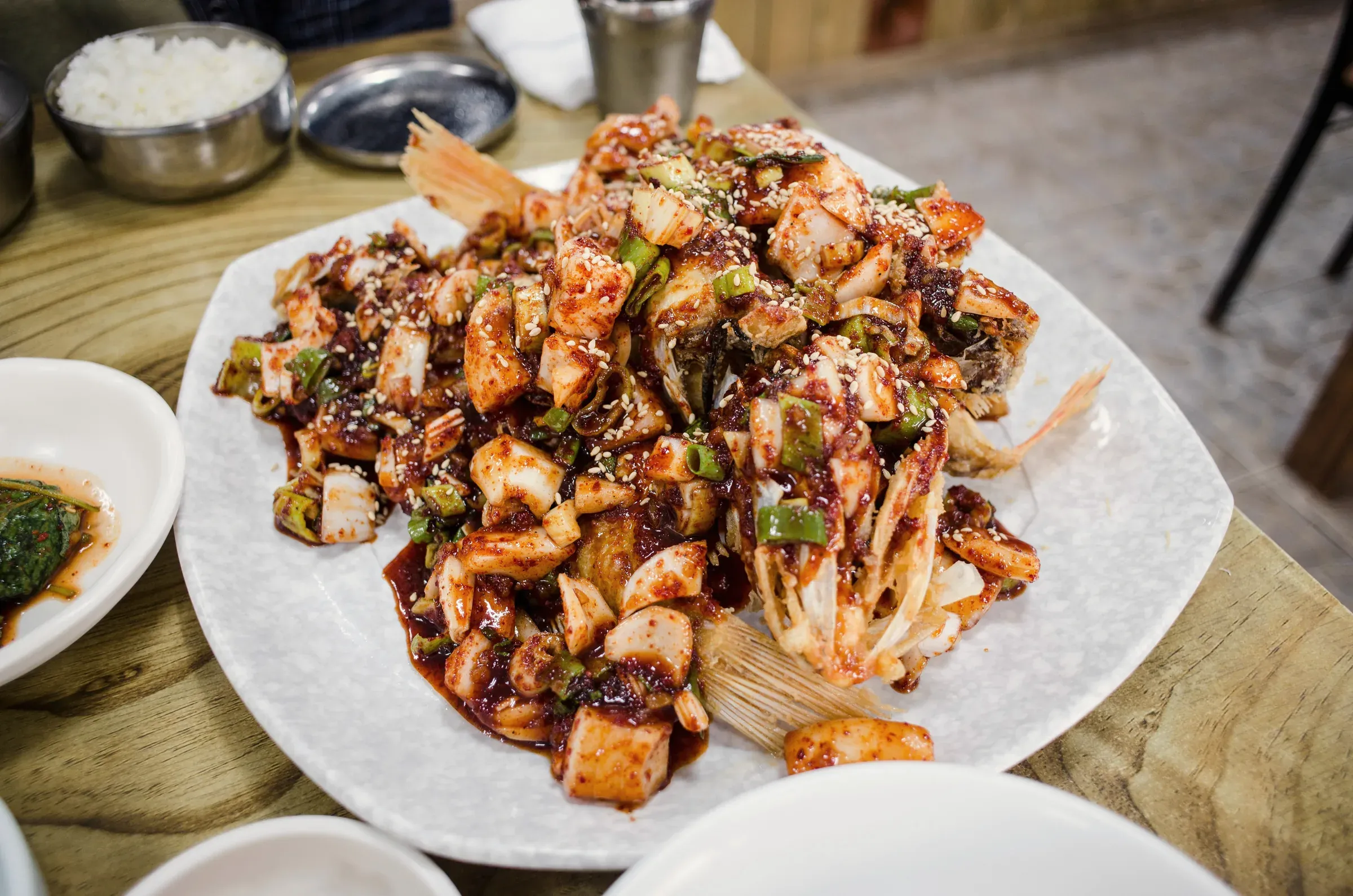 Braised pollock heaped with chili sauce, scallion and sesame on a white platter