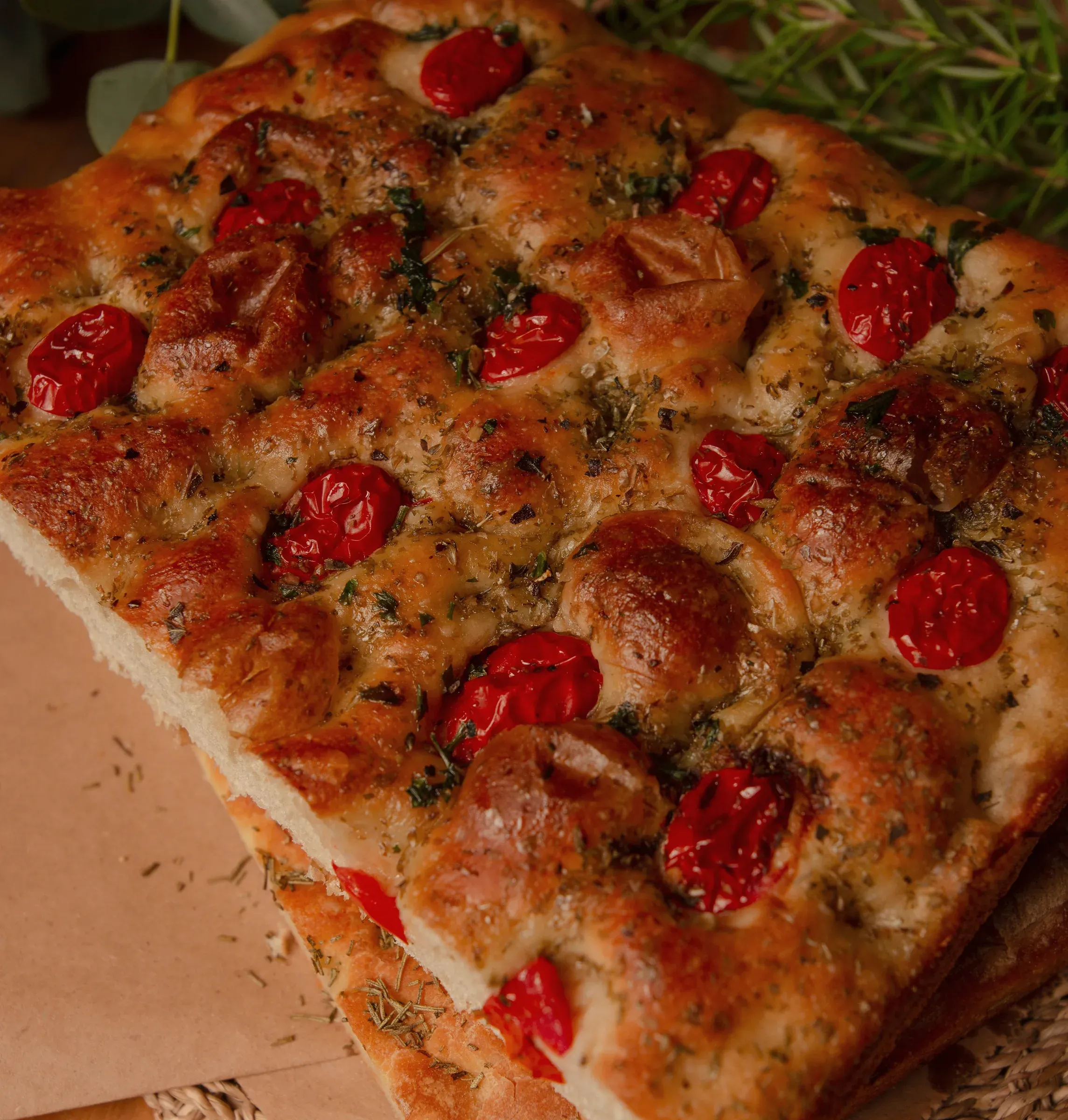 A slab of focaccia topped with cherry tomatoes and herbs