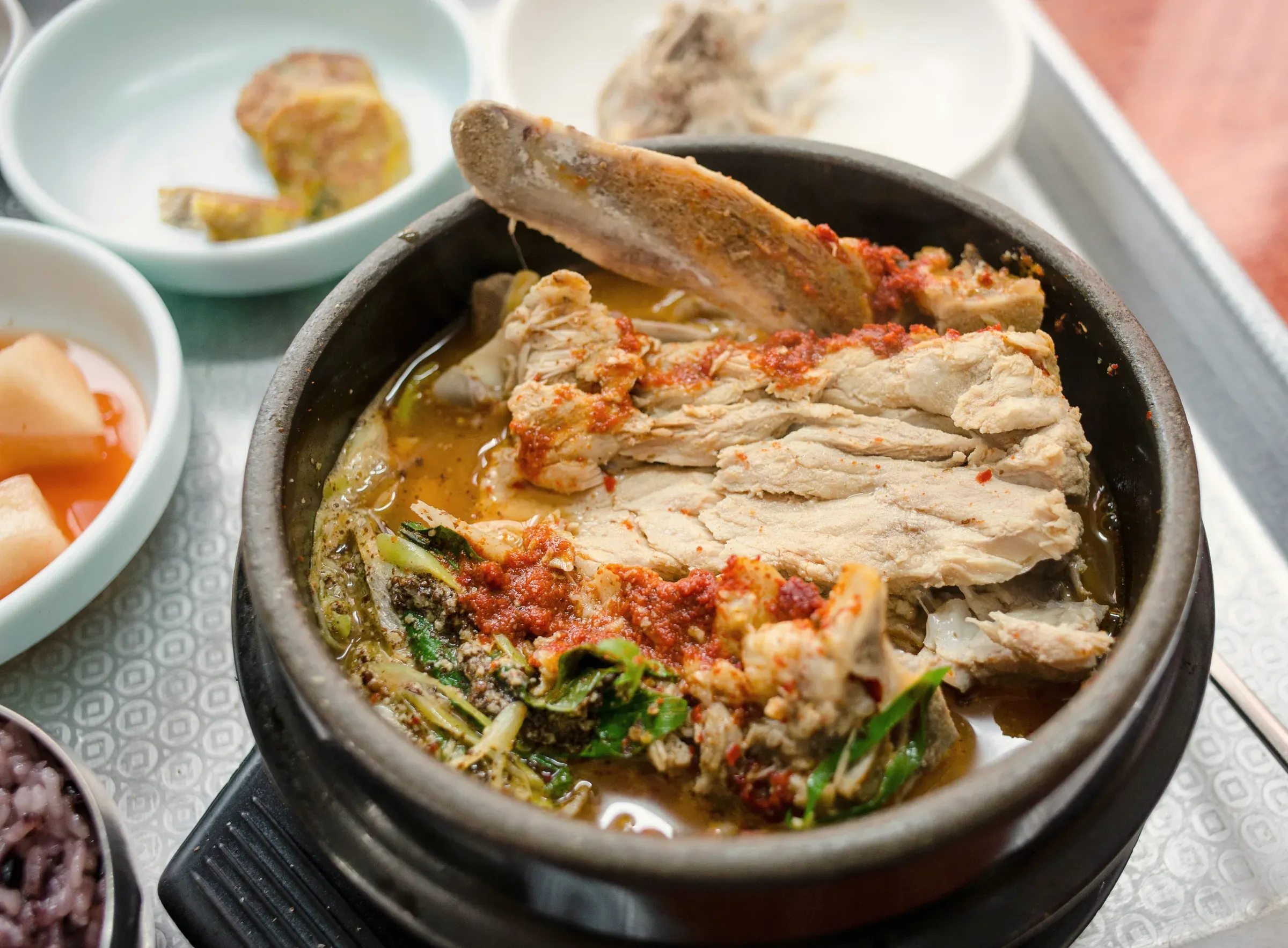 Pork bone stew in a black stone pot with banchan around it