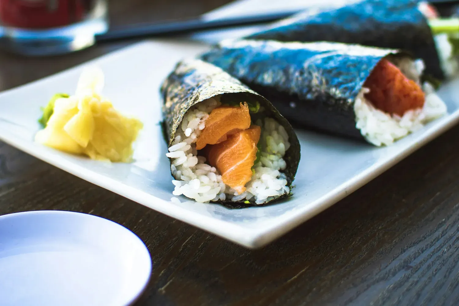 Two hand rolls on a white plate, one salmon and one spicy tuna, with pickled ginger