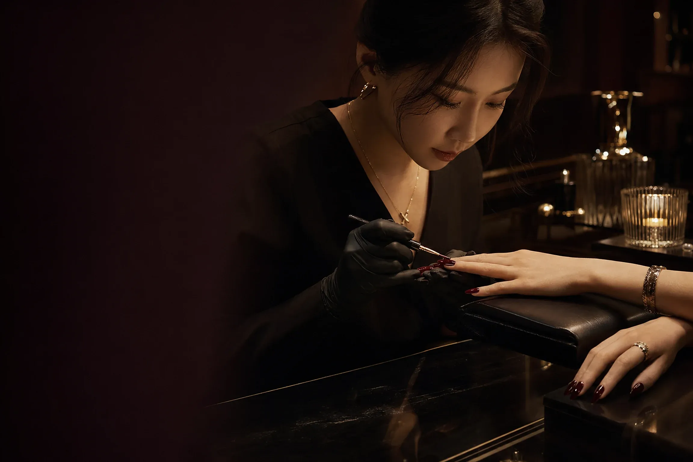A nail artist painting fine details on a client's nails by candlelight