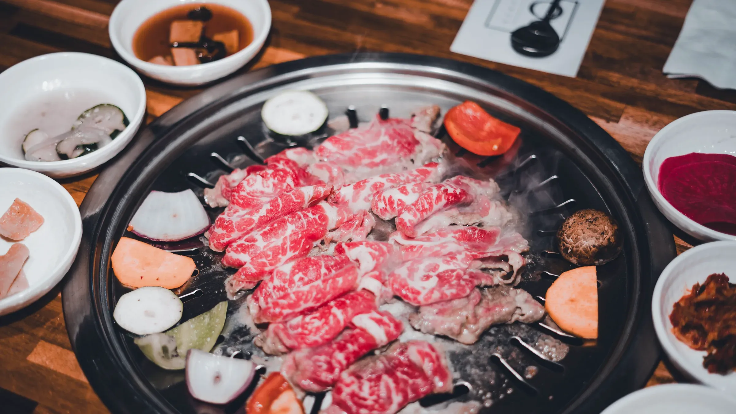 A charcoal grill packed with marbled beef, banchan bowls all around