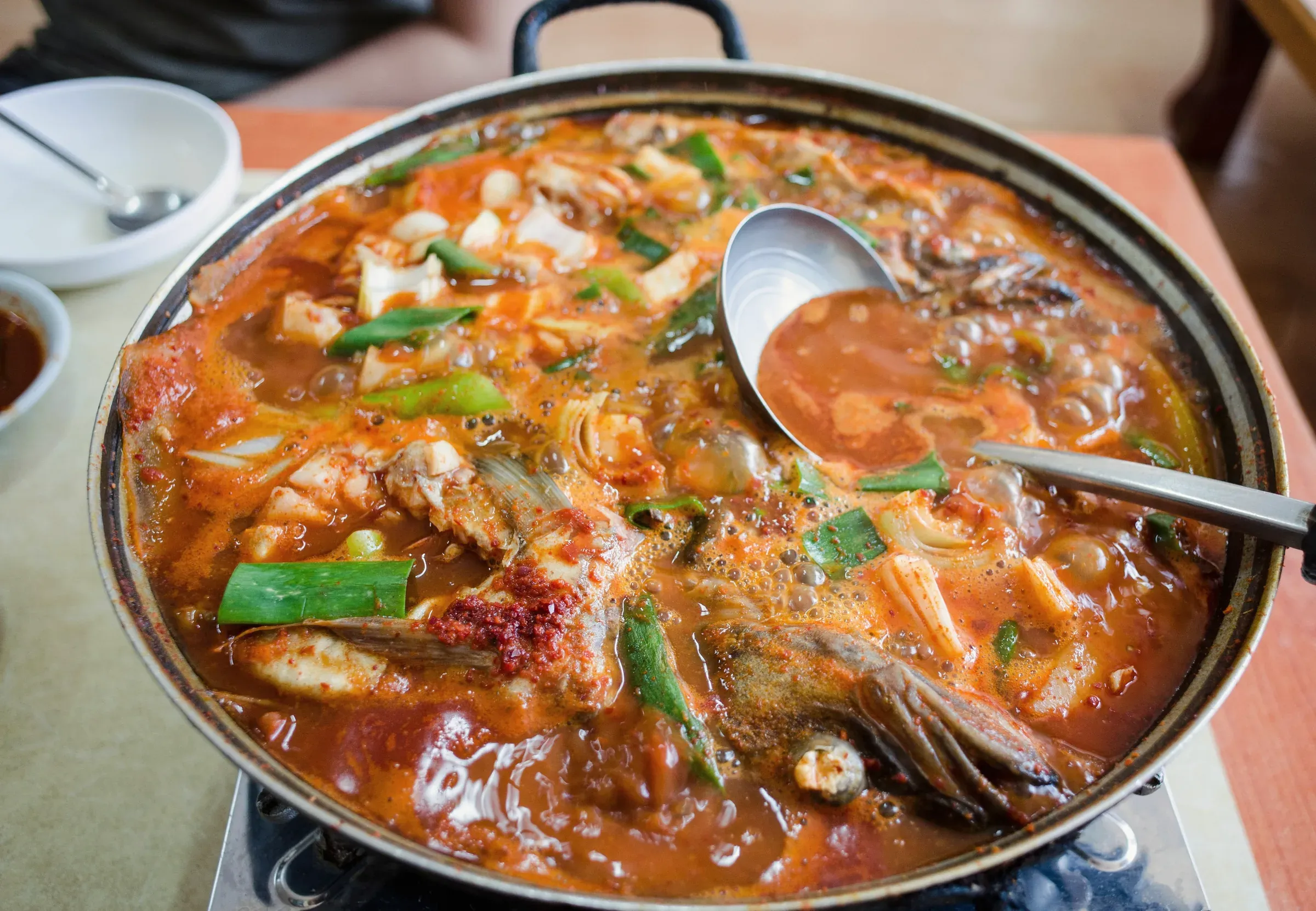 Seafood stew boiling in a wide pot on a table burner, a ladle resting in it