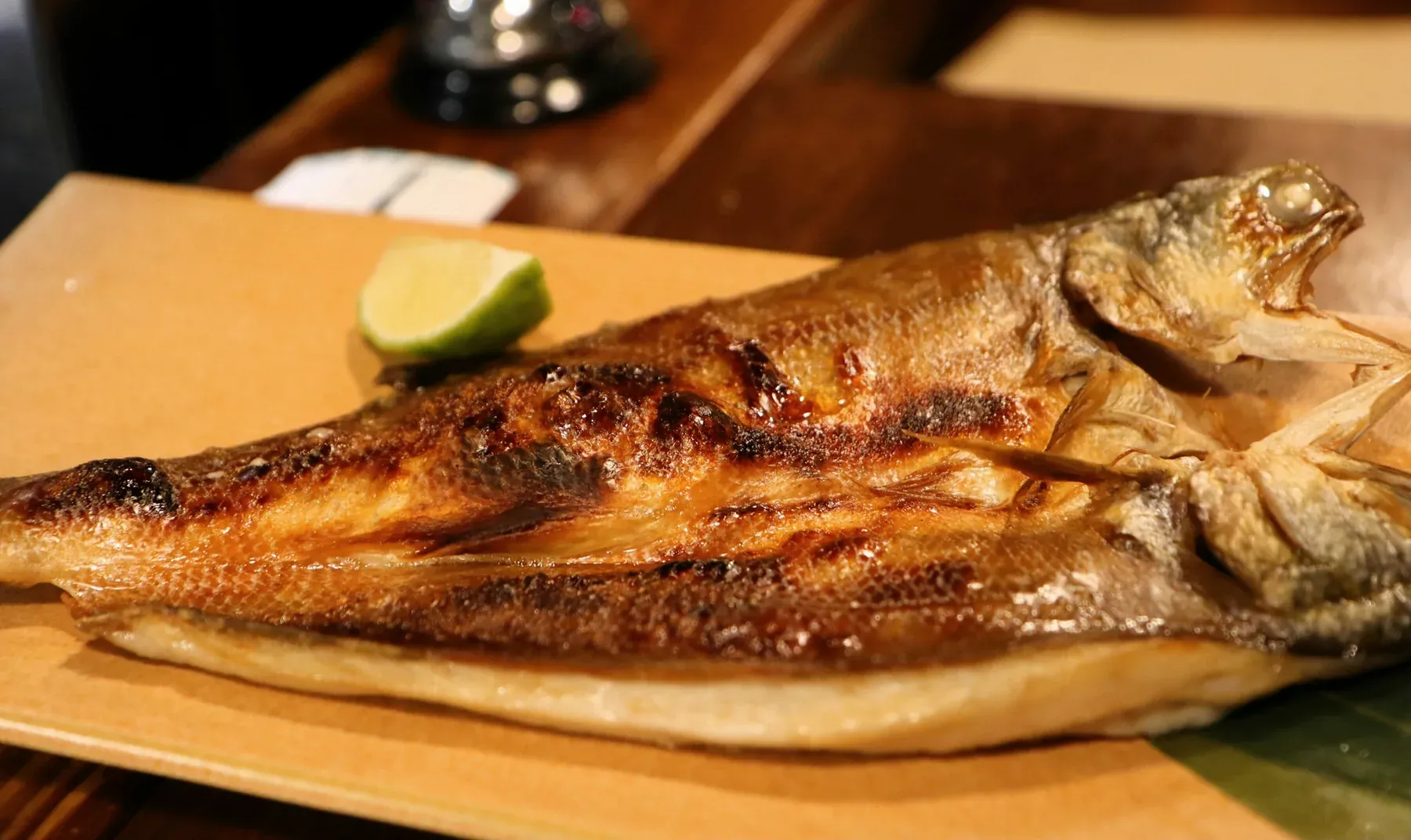 A whole split hokke, grilled golden, with a wedge of lime on a wooden board