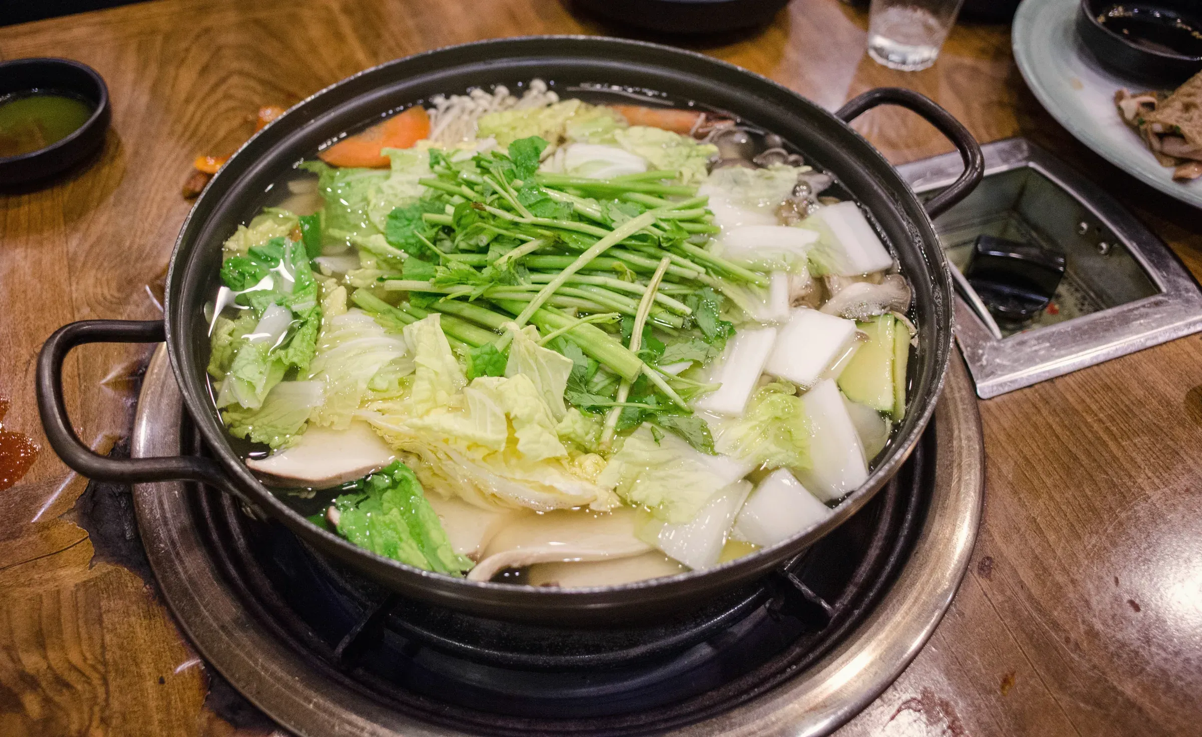 A mushroom and vegetable hot pot topped with crown daisy on a table burner