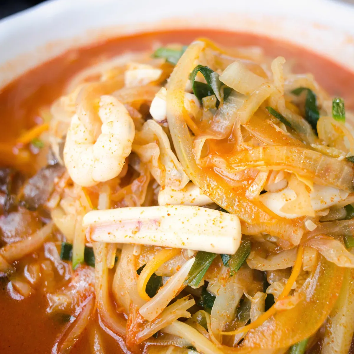 Red spicy seafood noodle soup with shrimp, squid, onion and chives