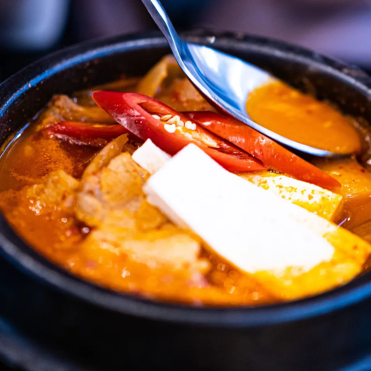 Red kimchi stew with tofu bubbling in a black stone pot