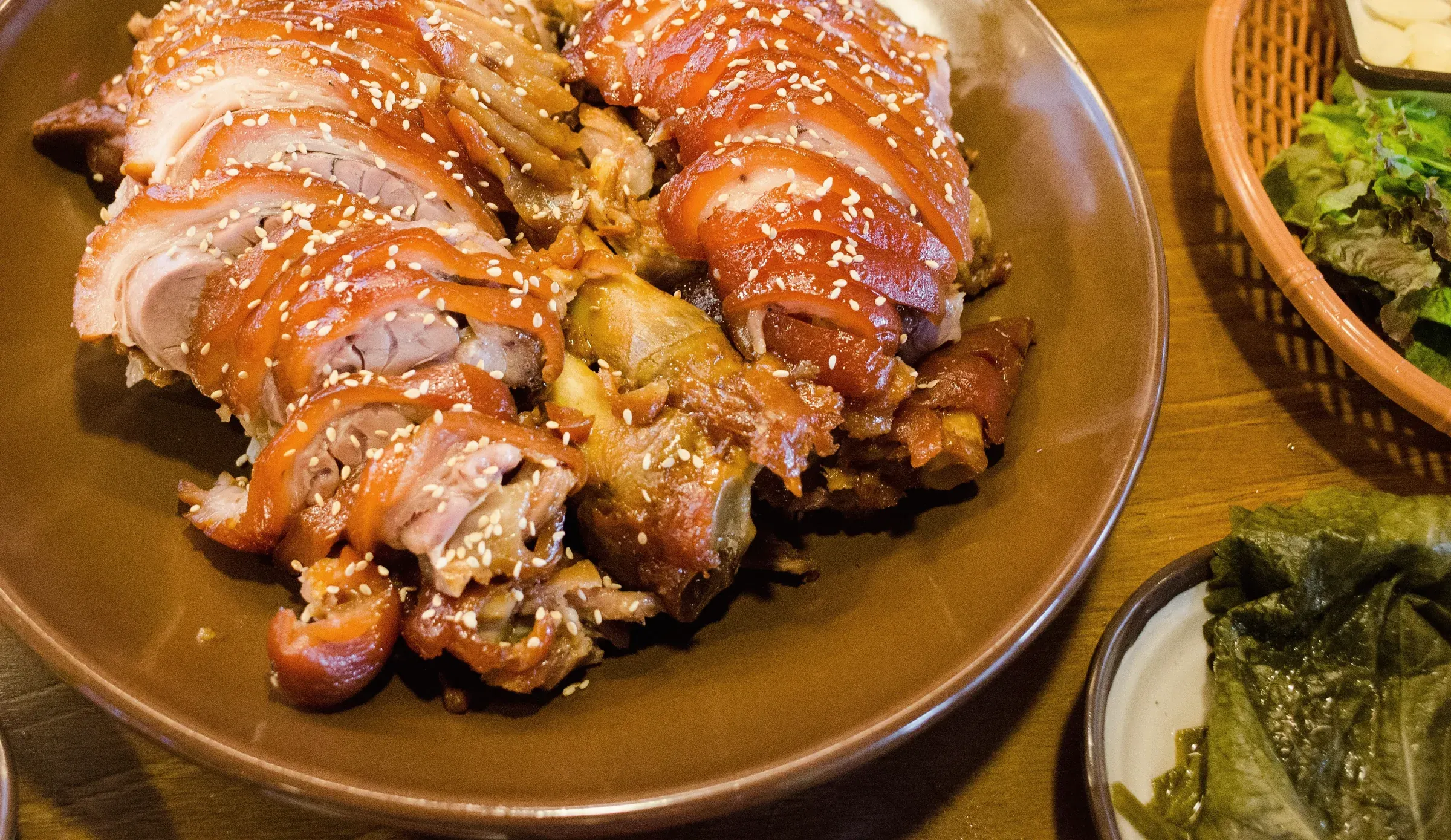 A platter of sliced jokbal with sesame, next to lettuce and garlic