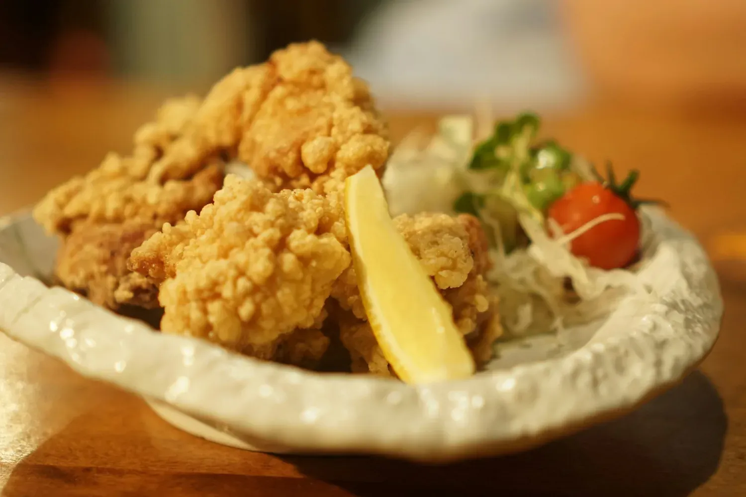 Fried chicken karaage with a lemon wedge, cabbage and a cherry tomato in a cream ceramic dish