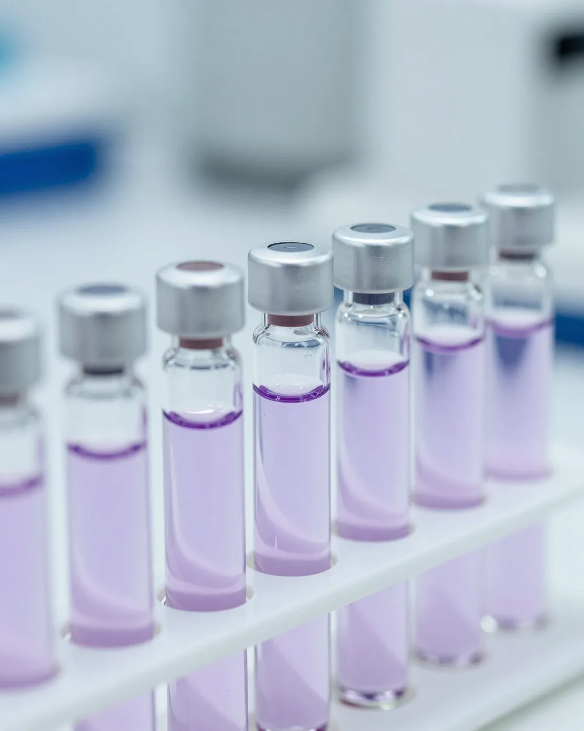 A rack of small glass vials holding clear to lilac liquids