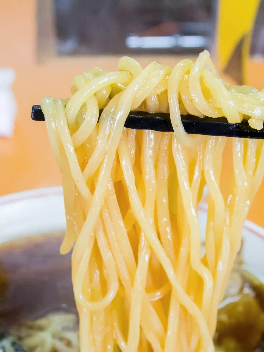 Medium wavy noodles lifted from a bowl with black chopsticks