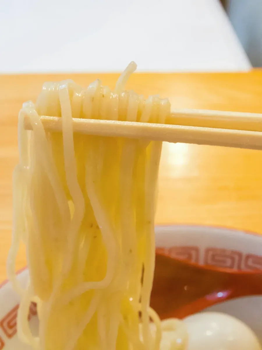 Thin straight noodles lifted from the bowl with wooden chopsticks