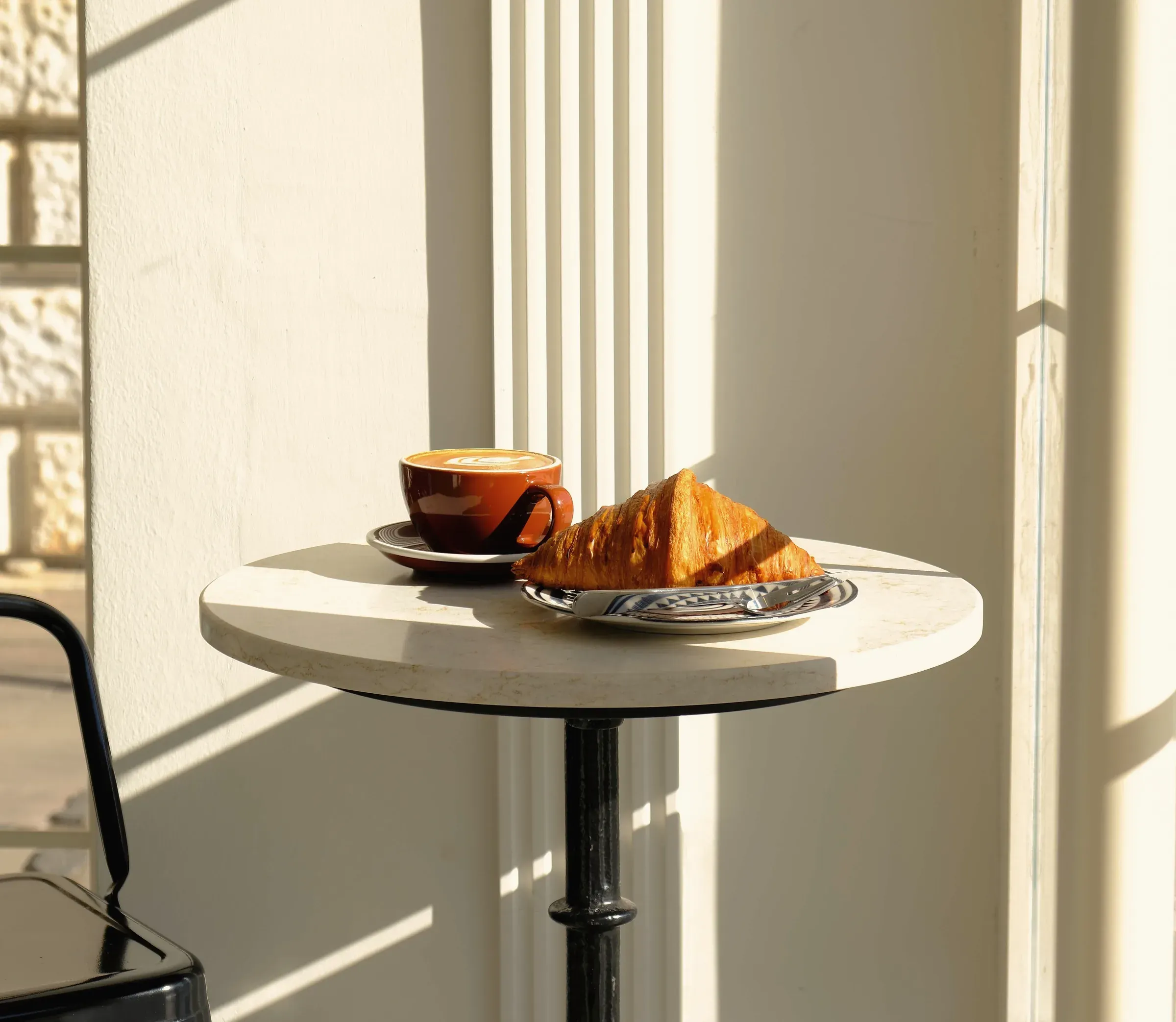 A croissant and coffee on a small table by the Long Beach window