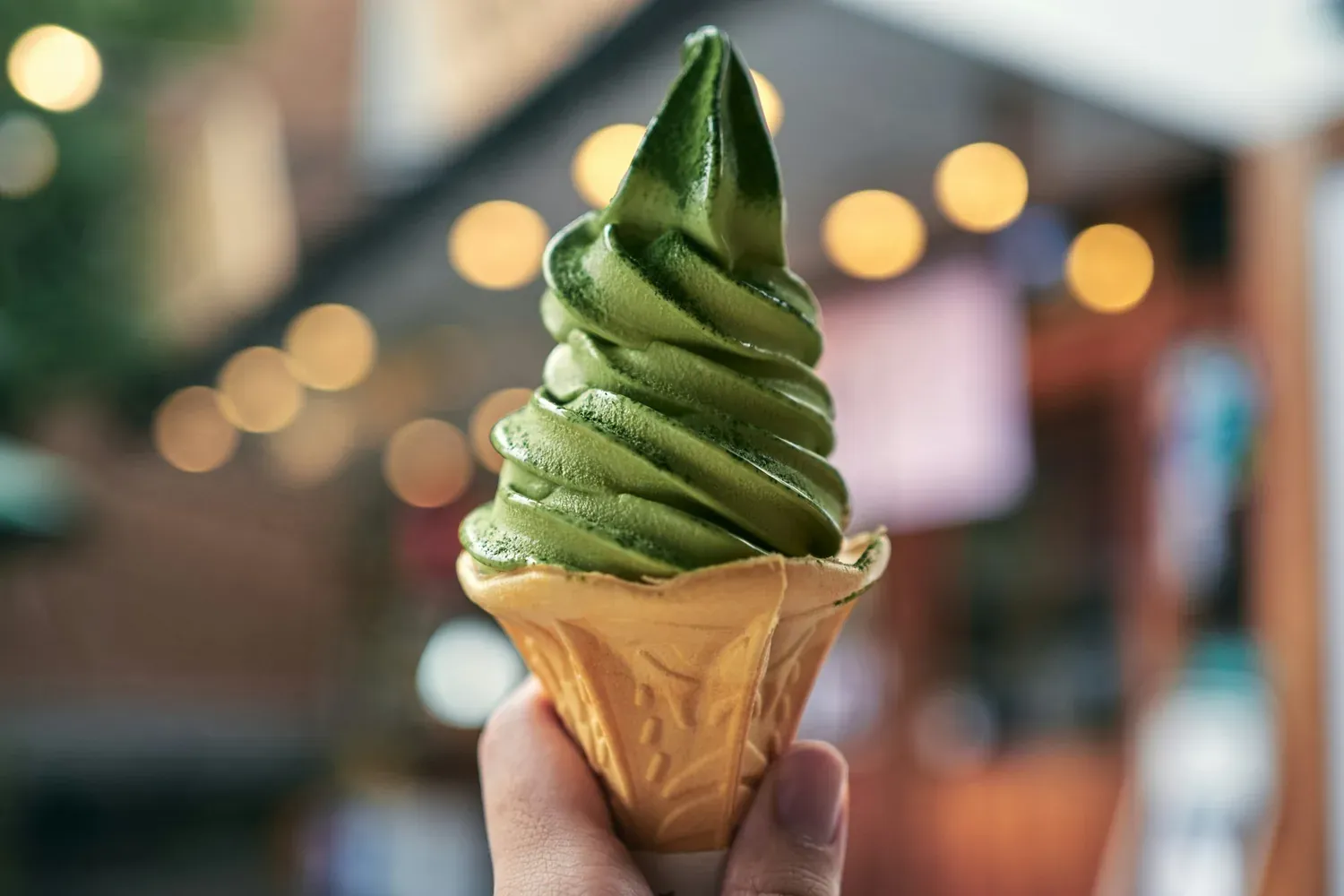 A hand holding a swirl of deep green matcha soft serve in a wafer cone