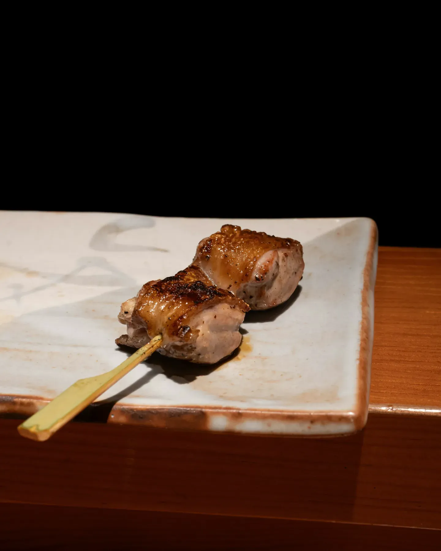 One chicken thigh skewer, charred at the edges, on a pale glazed plate