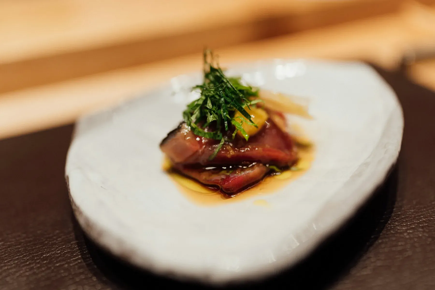 A course from the omakase counter: seared fish under shiso and a little sauce on a pale ceramic plate