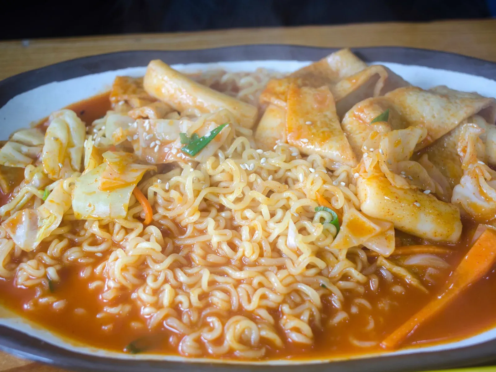 Ramen noodles, rice cakes, fish cake and cabbage mixed in red sauce on a black plate