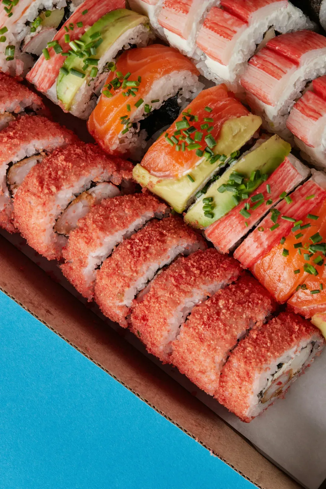 Rolls coated in red tempura crunch with shrimp tempura inside, packed in a to-go box on a blue table