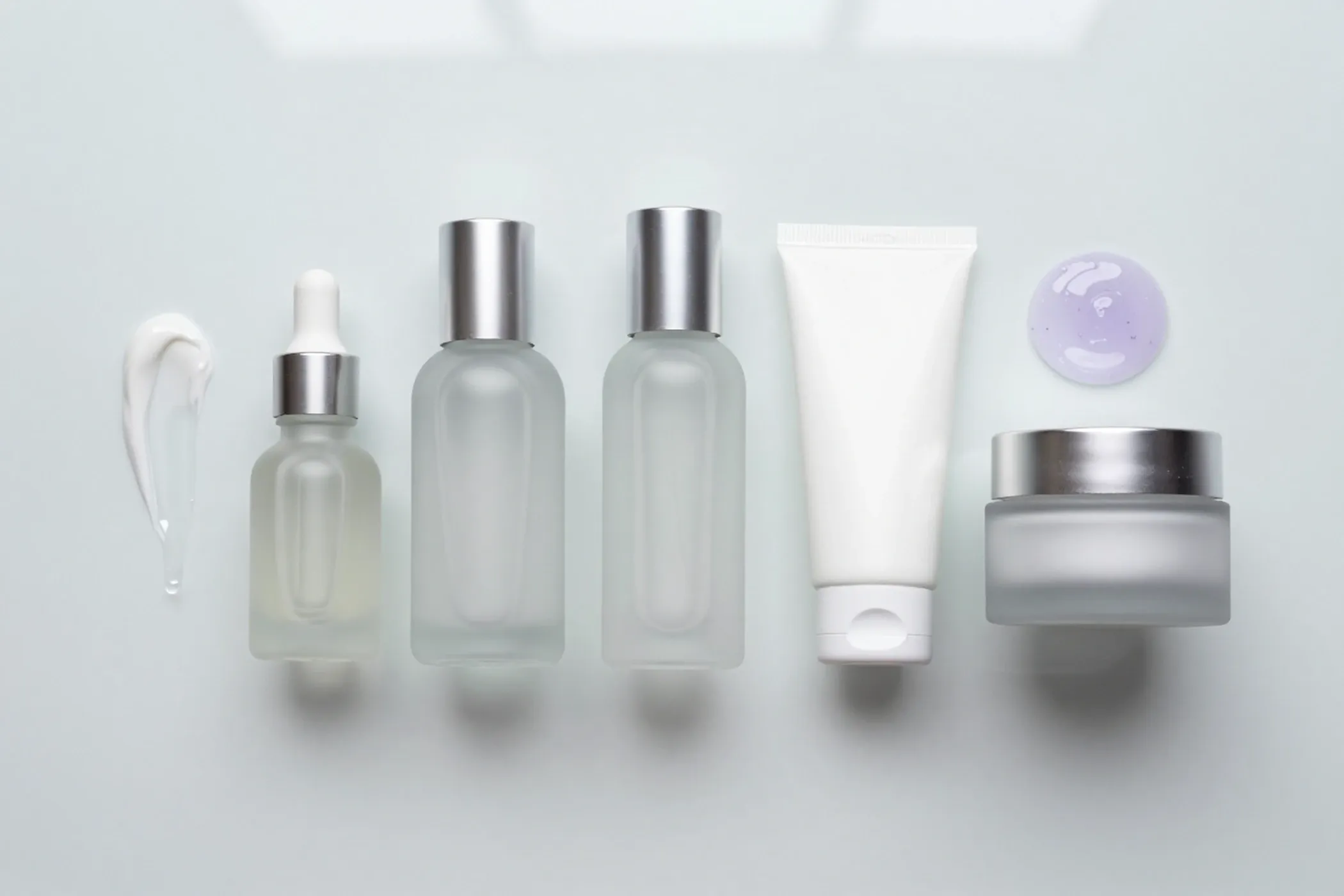 Frosted glass bottles and jars laid out in a row with swatches of serum and cream
