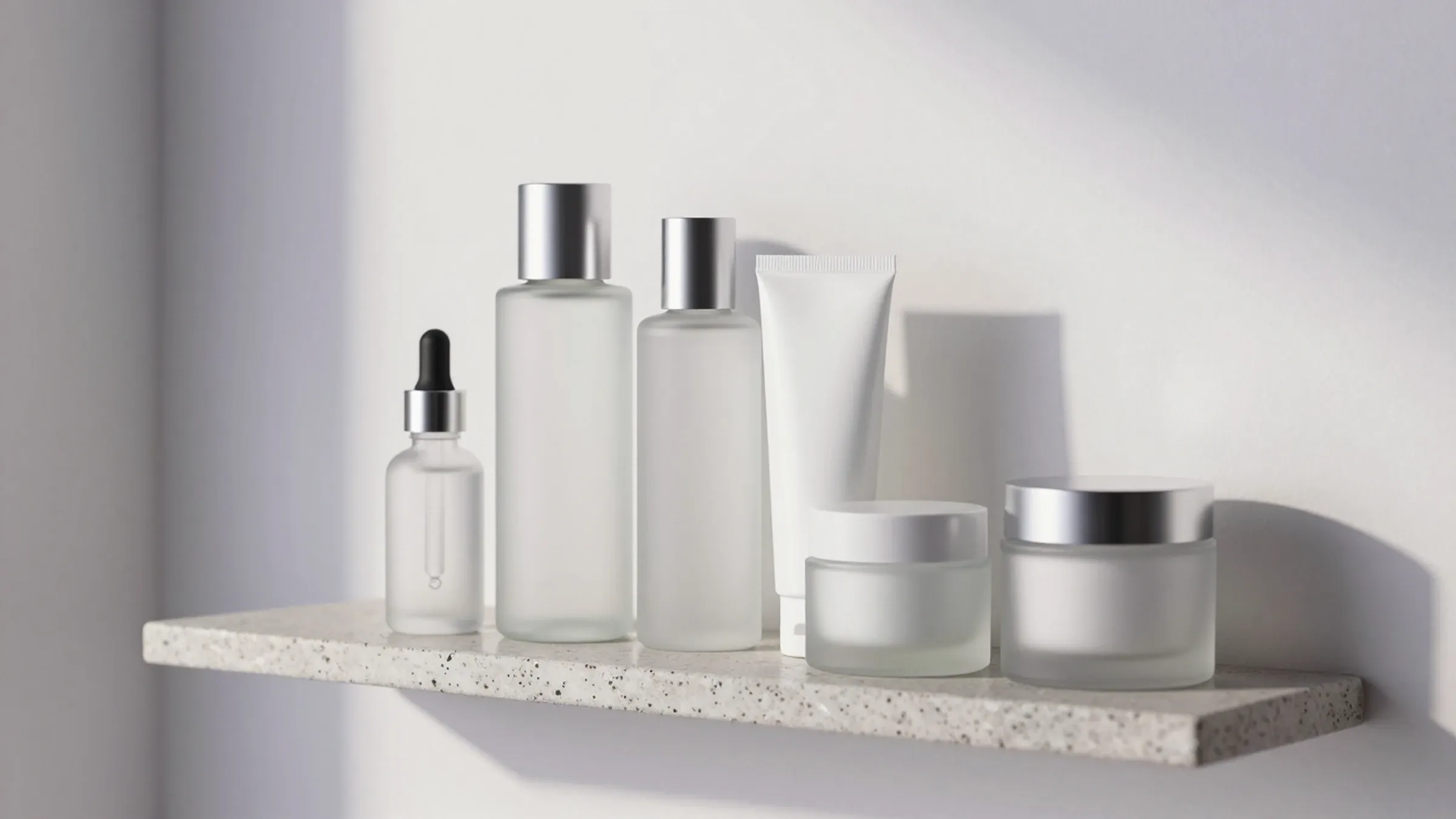 Five frosted glass products on a stone and glass bathroom shelf