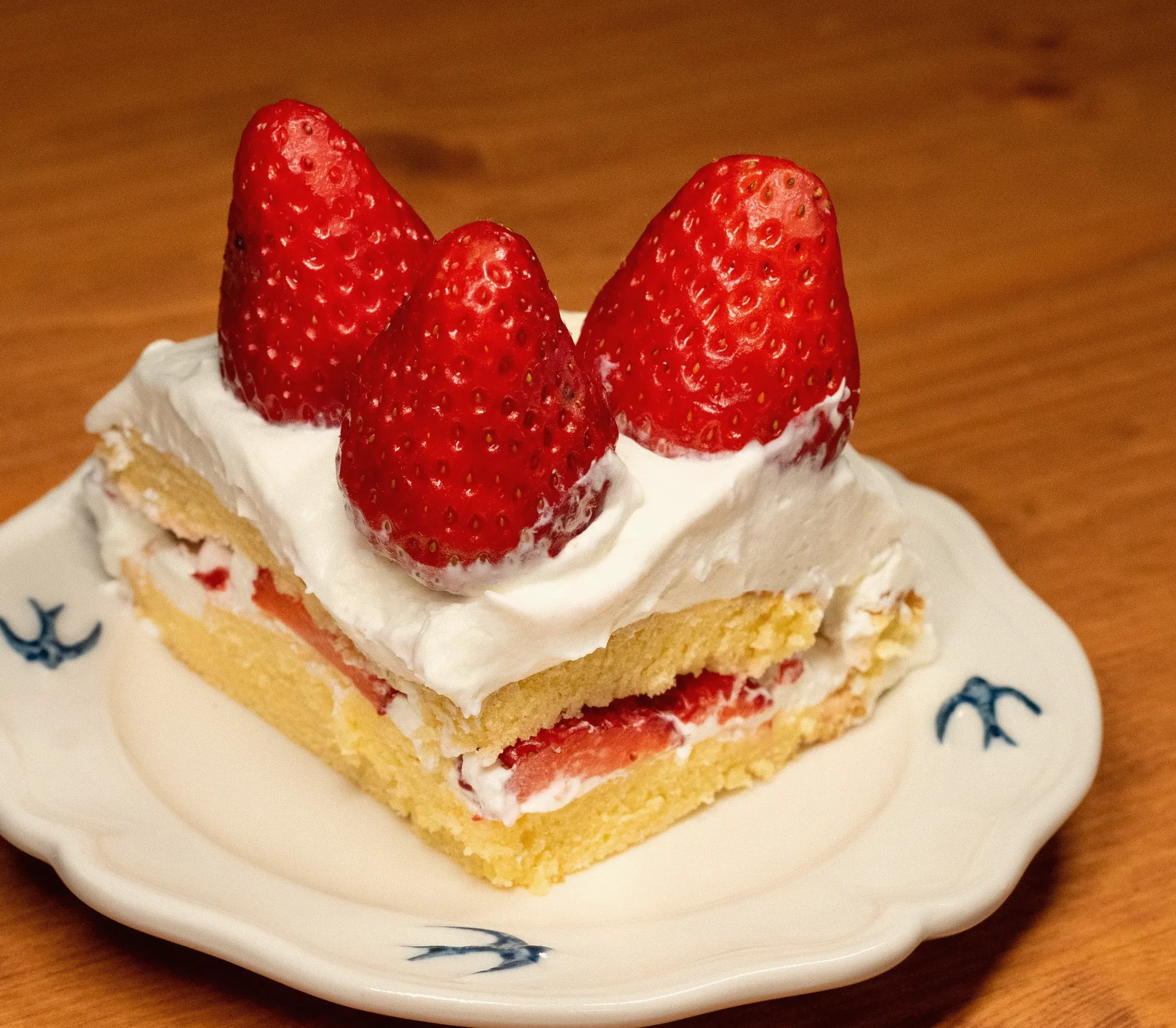 A slice of strawberry shortcake with three whole strawberries on top