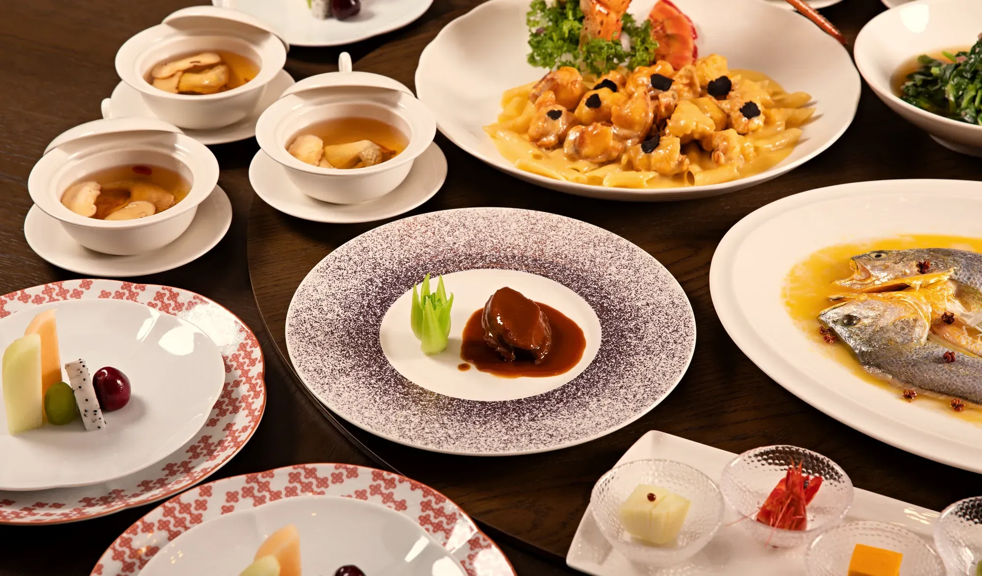 A banquet table: braised abalone, a steamed yellow croaker, lobster, soups and small plates