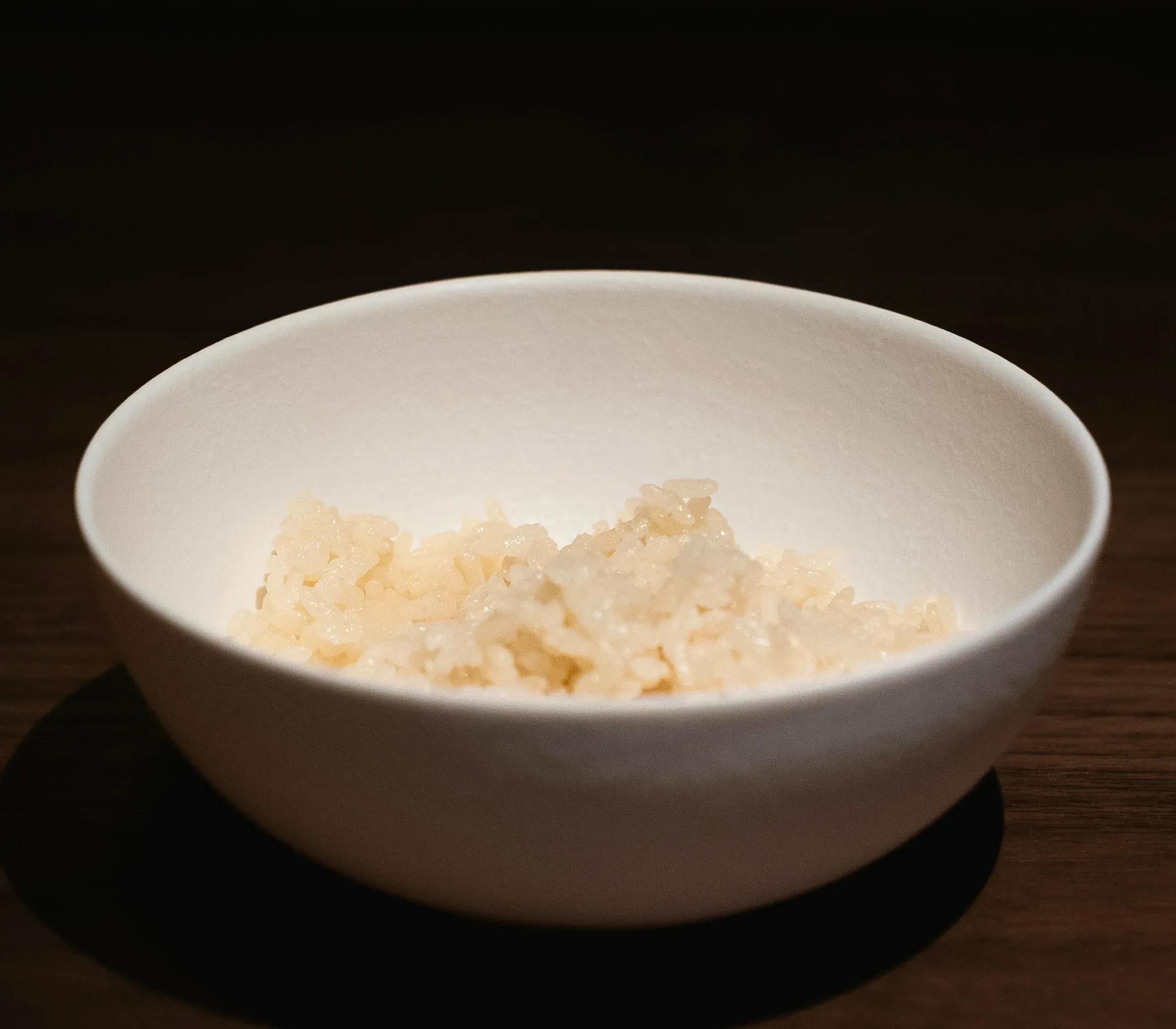Freshly cooked rice in a plain white bowl on a dark wood table
