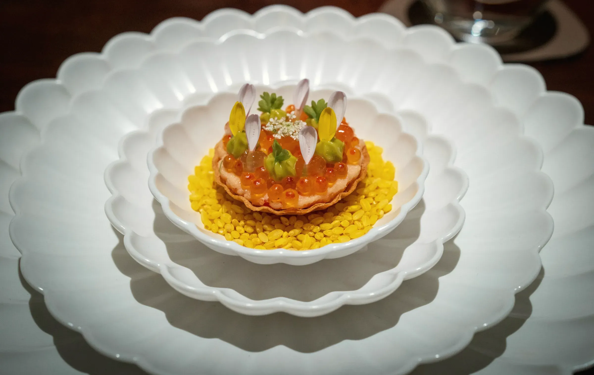 A salmon roe tart with petals and herbs on steamed barley, in a scalloped white porcelain bowl