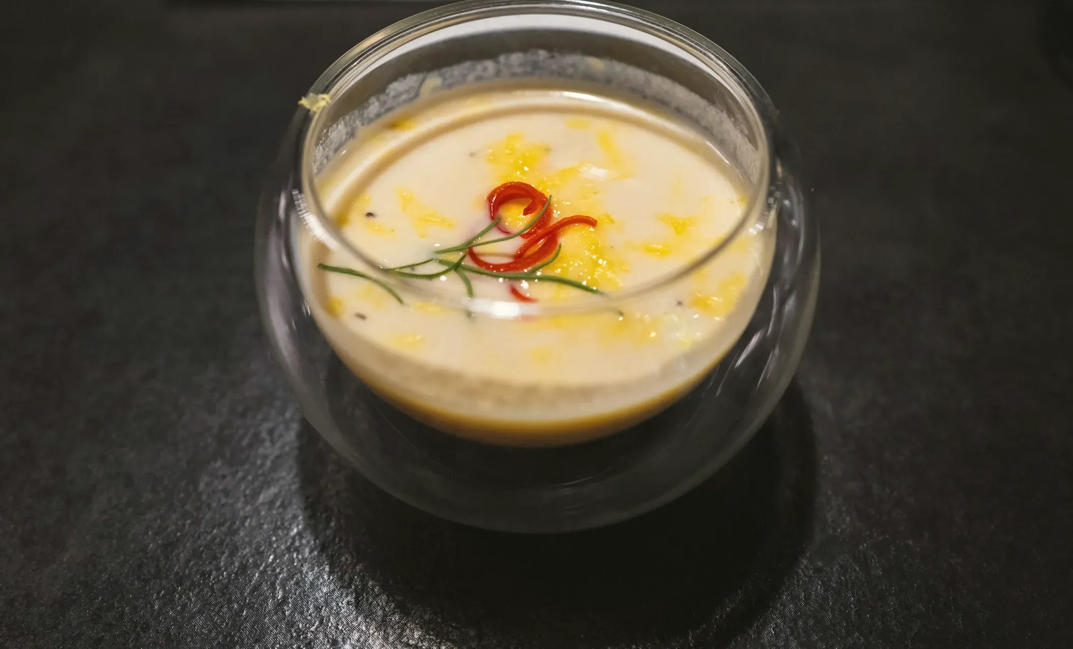 Chilled soy-milk soup with grated yolk and a curl of red chili in a double-walled glass bowl