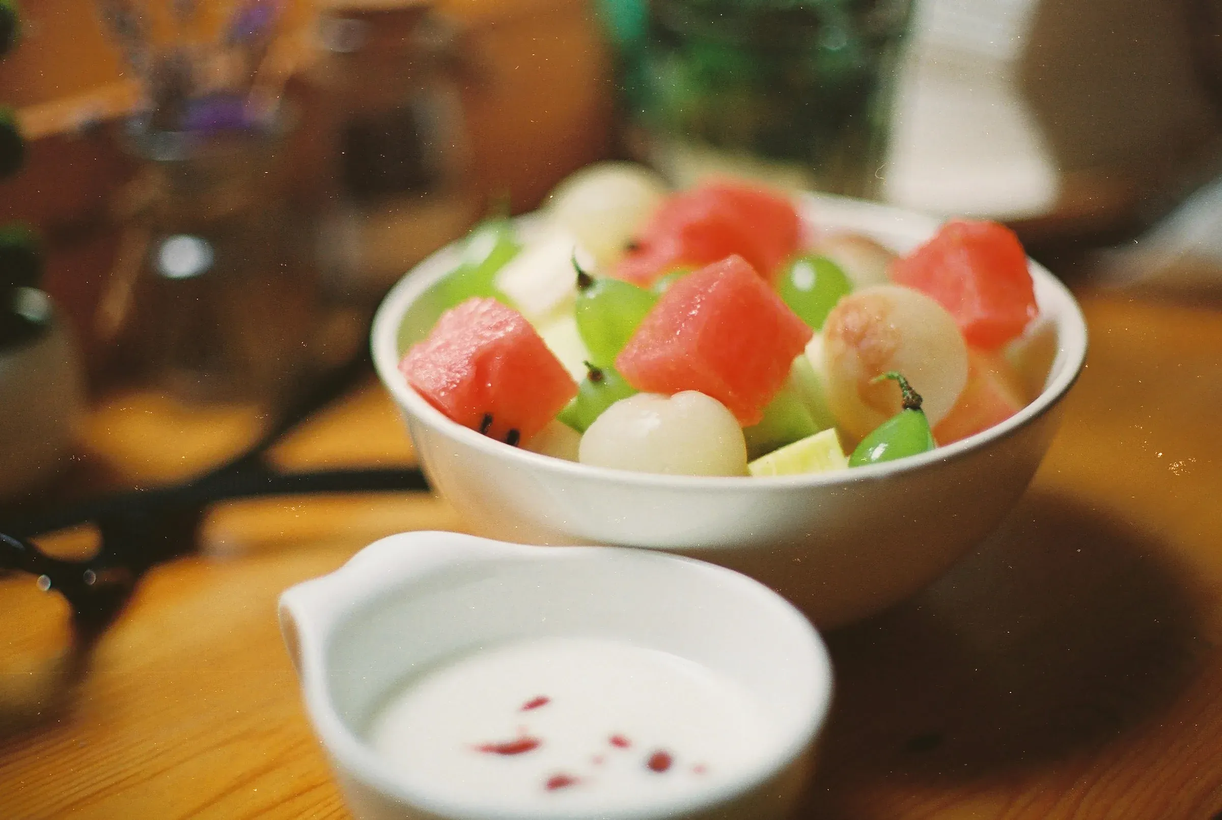 Watermelon, melon balls and green grapes in a white bowl, cold milk in a small jug beside it