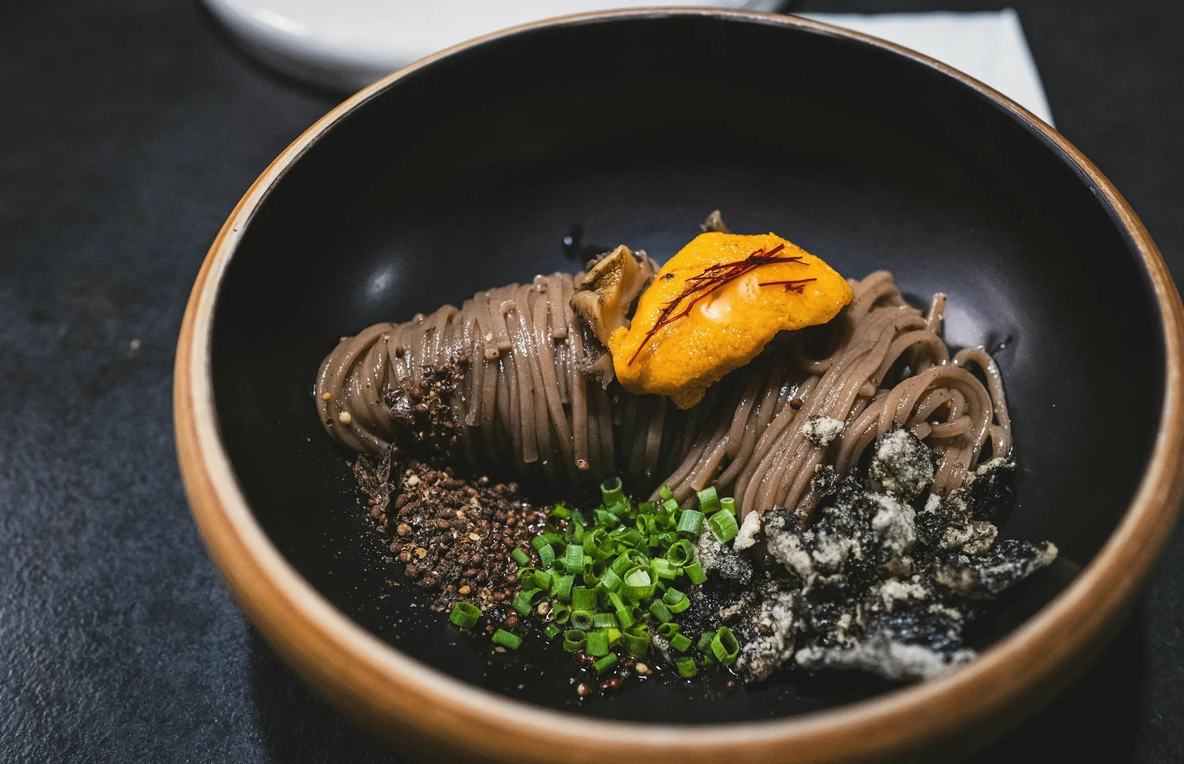Buckwheat noodles with sea urchin, chives and toasted grains in a brown stoneware bowl